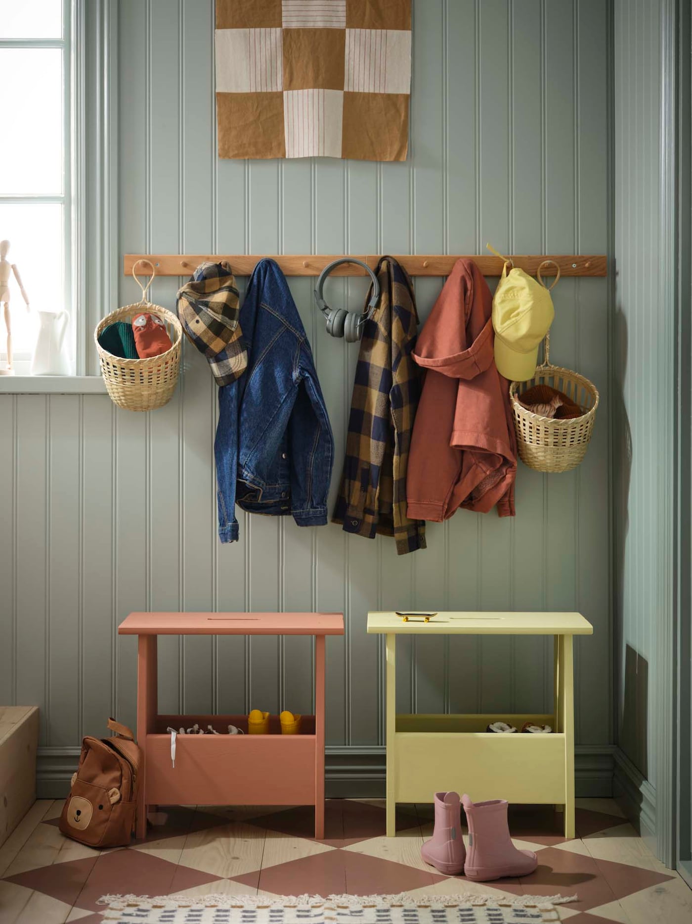 A green hallway with a yellow and terracotta PERJOHAN stool and clothes hanging on a coat rail above.