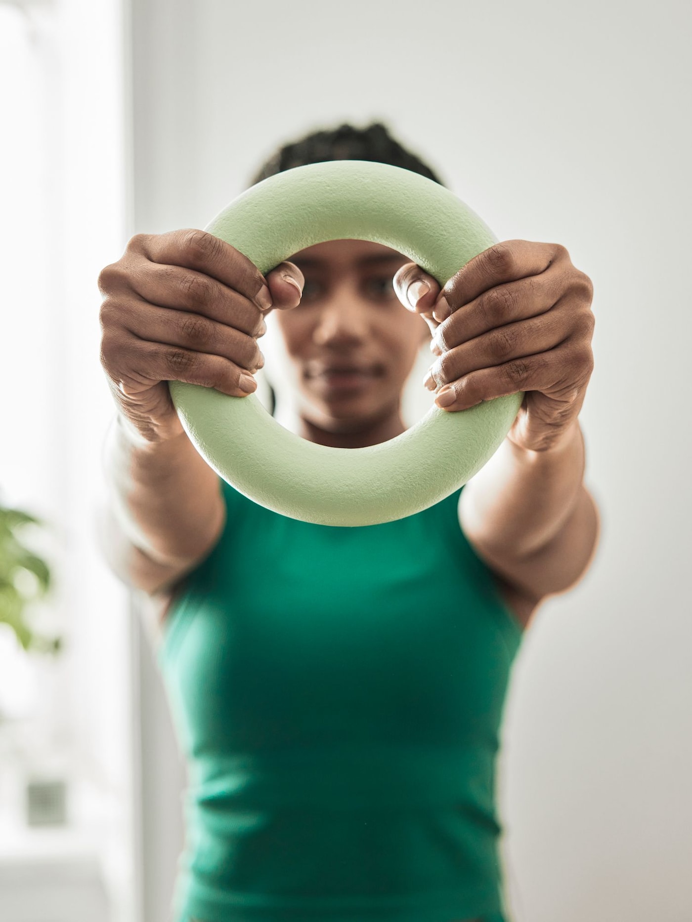 A young woman in a green vest holds a training ring in front of her. She is looking through the ring as she trains.