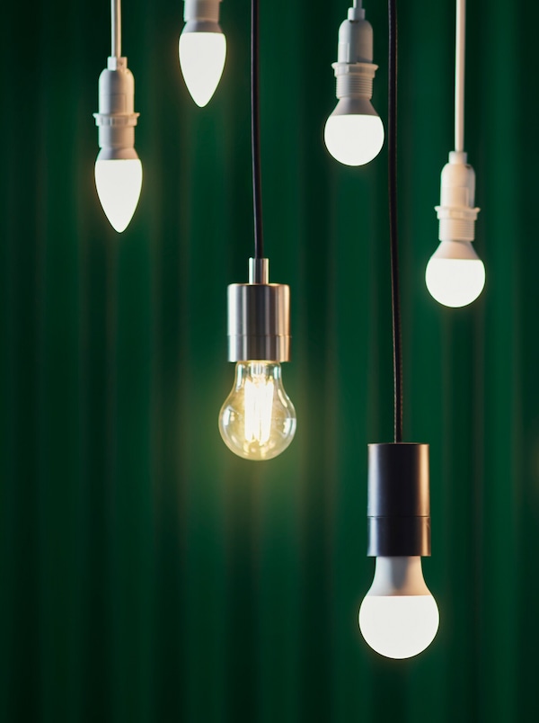 Six LED bulbs in various designs hung at different heights against the backdrop of a dark green curtain.