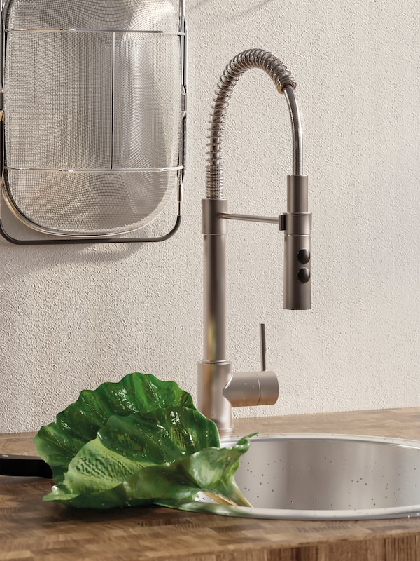 Stainless steel VIMMERN kitchen mixer tap with handspray at a round BOHOLMEN inset sink, green leaves on the edge.